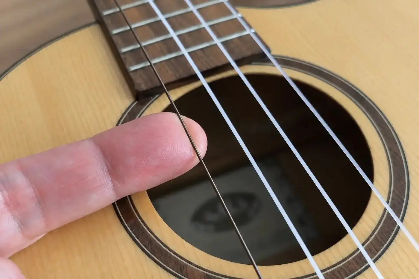 Ein Finger zupft die umsponnene Low-G-Saite einer Tenor-Ukulele am Schallloch