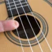 Ein Finger zupft eine Saite einer Konzert-Ukulele am Schallloch.