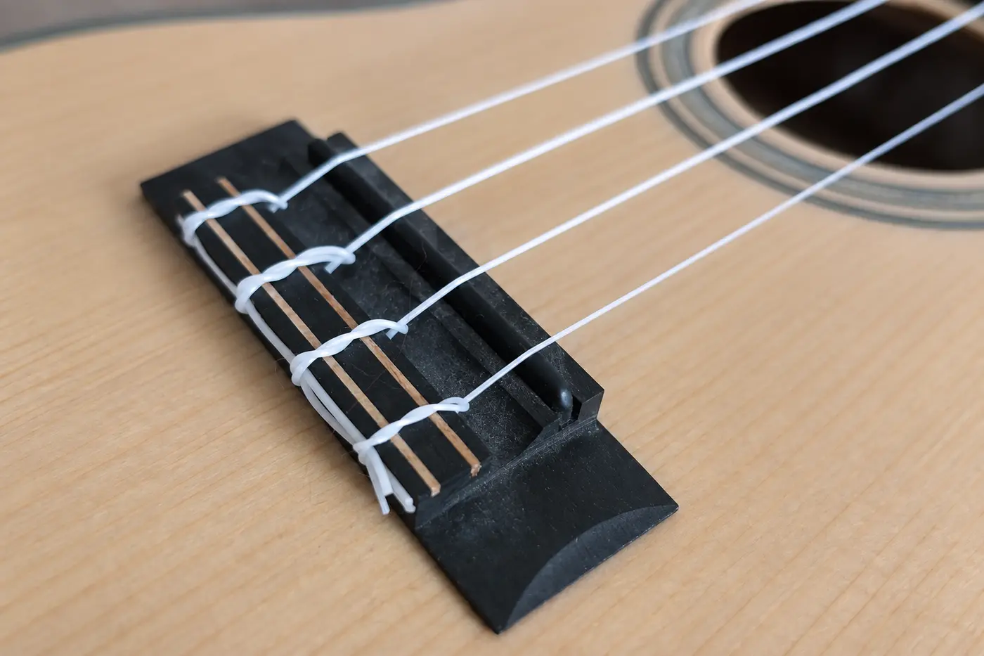 Vier weiße Ukulele-Saiten sind mit Knoten am Steg einer Konzert-Ukulele befestigt